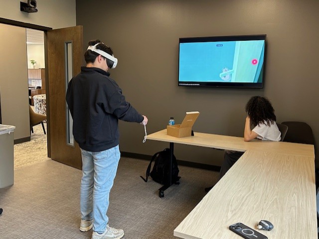 one person engaging in a virtual reality program and another person watching the screen